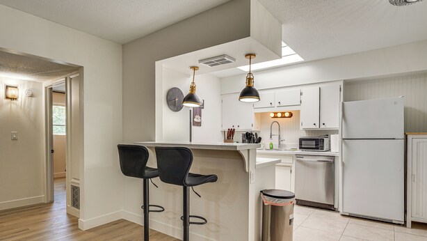 A modern kitchen with white cabinets, a stainless steel trash can, two black bar stools, and pendant lights. - Summer-Ready Old Town Condo w/ Pool & Patio Access (Scottsdale)
