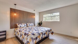 A modern bedroom with a large bed, a wooden slat wall, a window, and a bedside table. - Summer-Ready Old Town Condo w/ Pool & Patio Access (Scottsdale)
