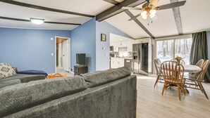 Un salon avec un canapé, une table à manger et des chaises, un ventilateur de plafond, et un coin cuisine visible à travers une porte ouverte.