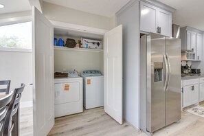 Eine kompakte Küche mit Edelstahl-Kühlschrank, integriertem Wasch- und Trockner sowie weißen Schränken.