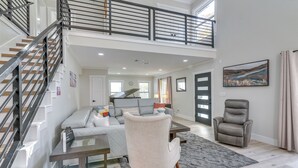 A spacious living area with a staircase, a gray sofa, a recliner, and a painting on the wall. - Home 2 Mi to Hermann Park, Zoo & Museum District! (Houston)