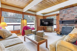 A cozy living room with a fireplace, large windows, and a television.