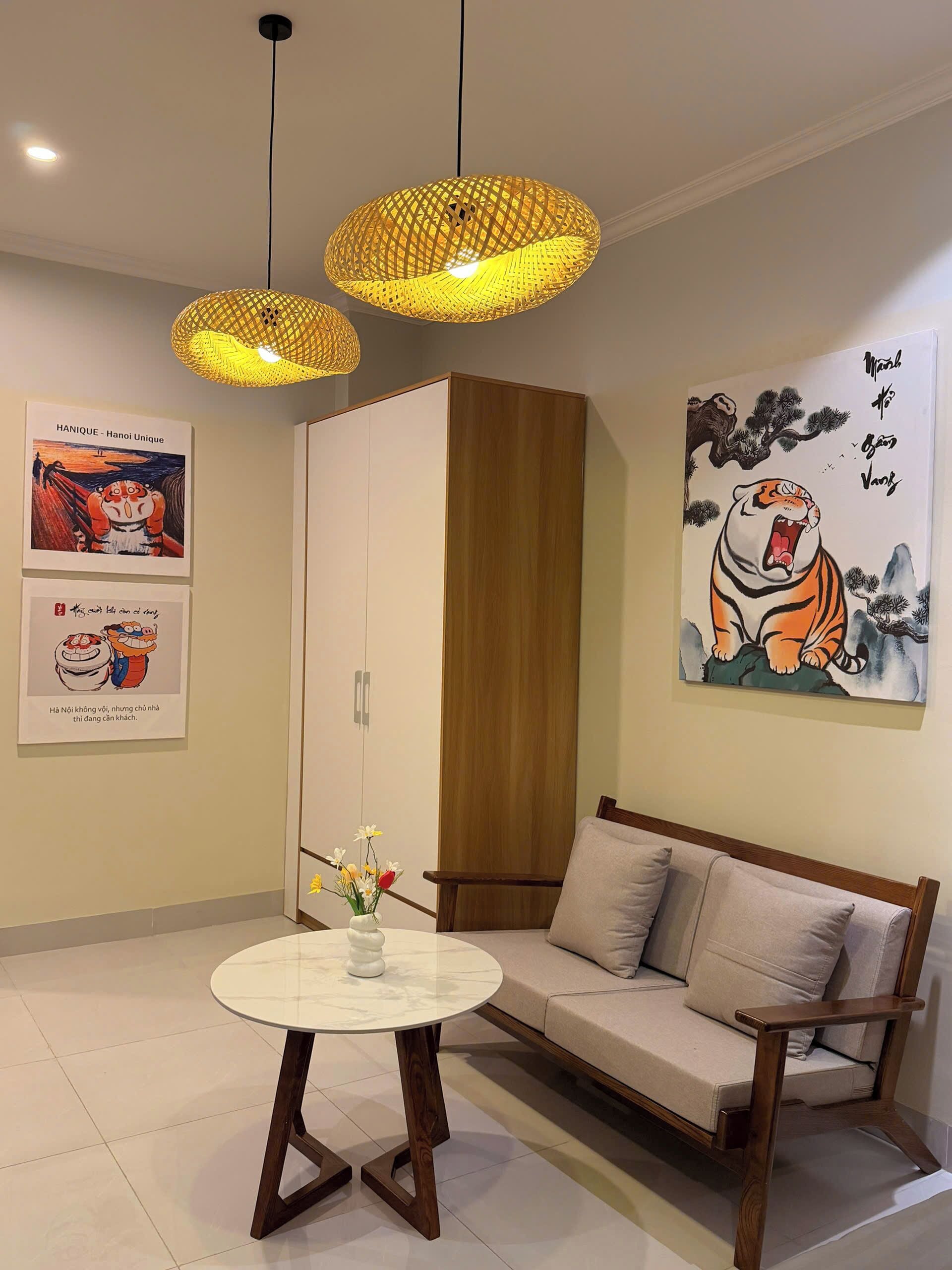 A modern living room with a sofa, a round coffee table, and two hanging lamps. There are framed artworks on the walls and a cabinet.
