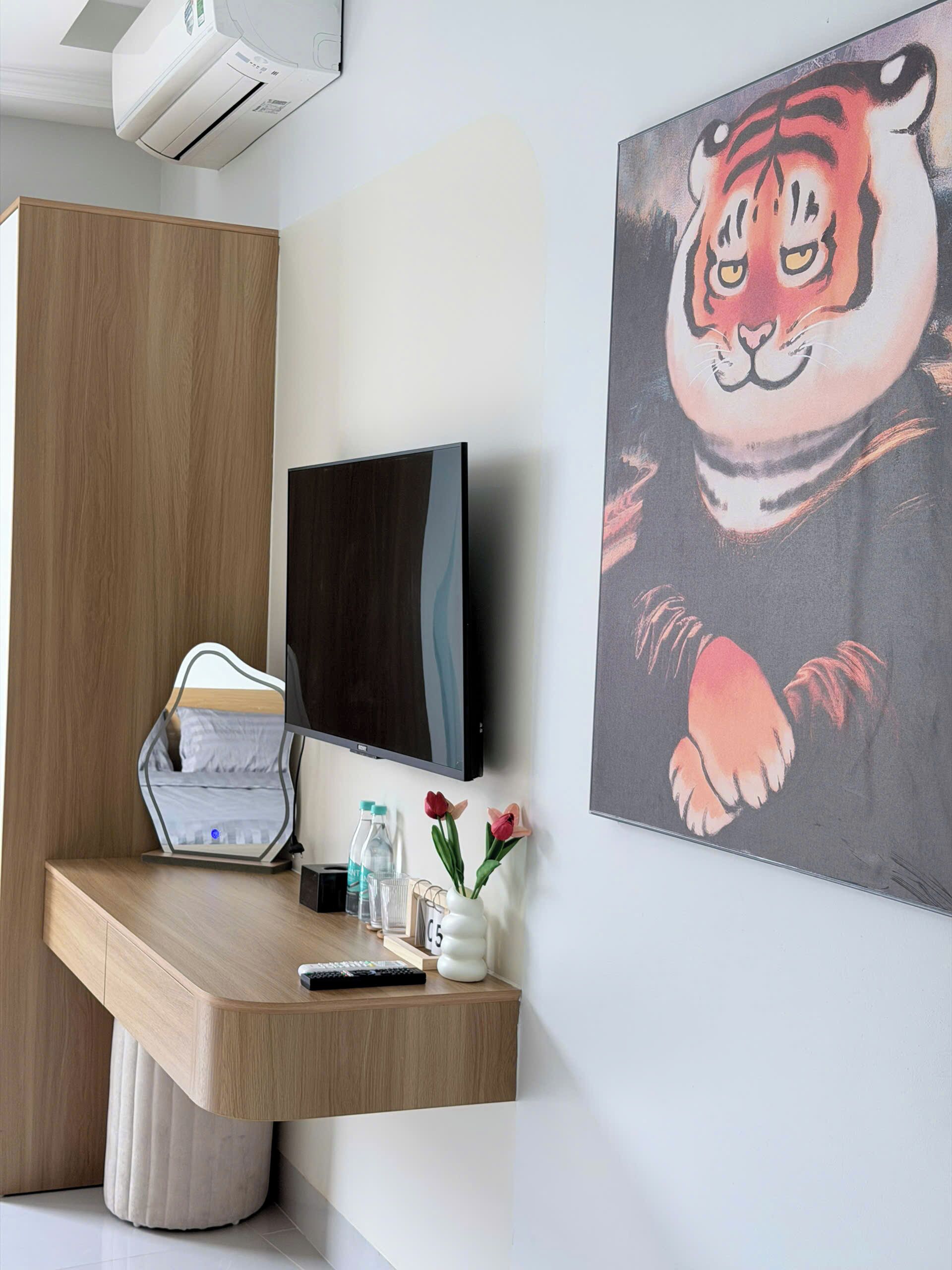 Une chambre moderne dotée d’un bureau en bois, d’un téléviseur à écran plat, d’un lit avec une tête de lit, d’un climatiseur mural et d’un grand tableau représentant un tigre.
