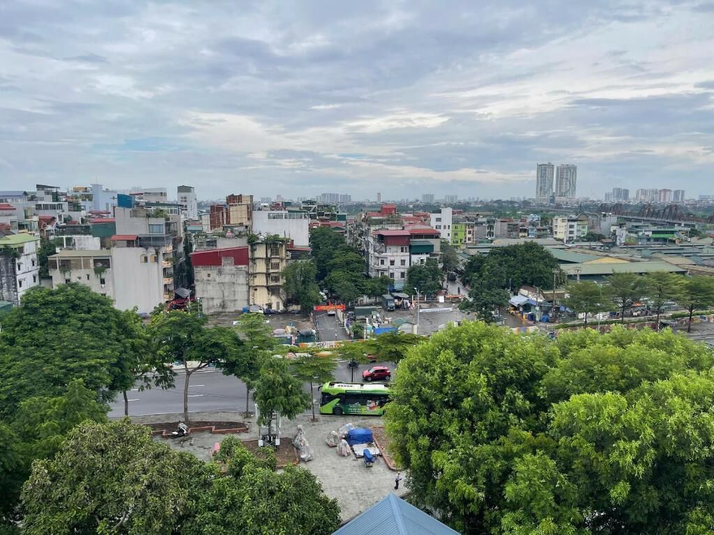 A cityscape with a variety of buildings, including residential and commercial structures. There is a green bus in the foreground, and the area appears to be a mix of urban and green spaces.