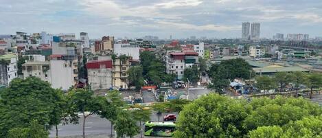 A cityscape with a variety of buildings, including residential and commercial structures. There is a green bus in the foreground, and the area appears to be a mix of urban and green spaces.