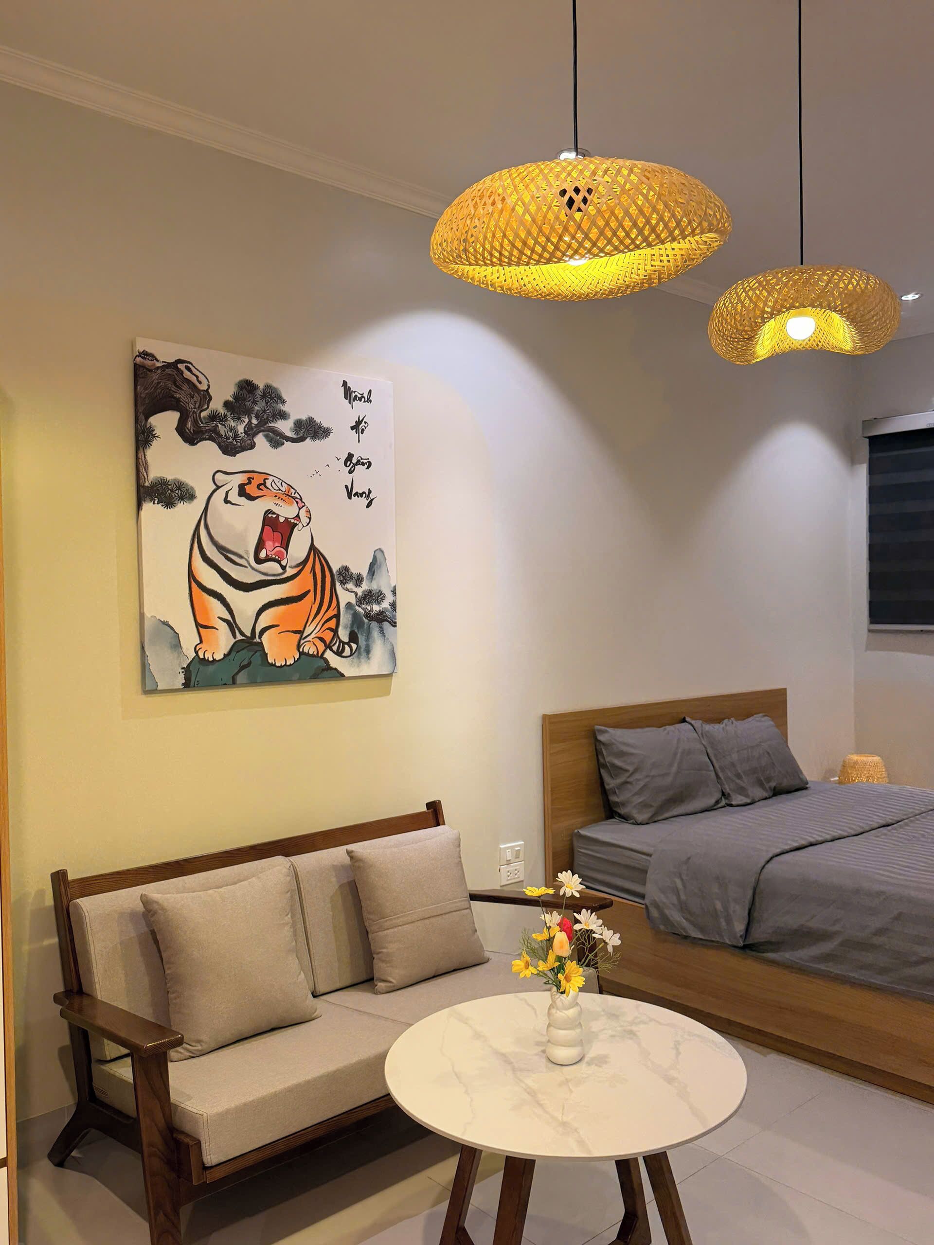 Een moderne slaapkamer met een bank, een bed, een ronde tafel met een bloemenvaas, en een schilderij van een tijger aan de muur.