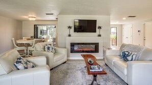 A living room with a fireplace, white sofas, a coffee table, and a TV mounted above the fireplace. - Port Charlotte Home w/ Heated Pool & Yard! (Port Charlotte)