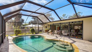 A covered outdoor swimming pool with a patio area, a glass enclosure, and a view of the surrounding landscape. - Port Charlotte Home w/ Heated Pool & Yard! (Port Charlotte)