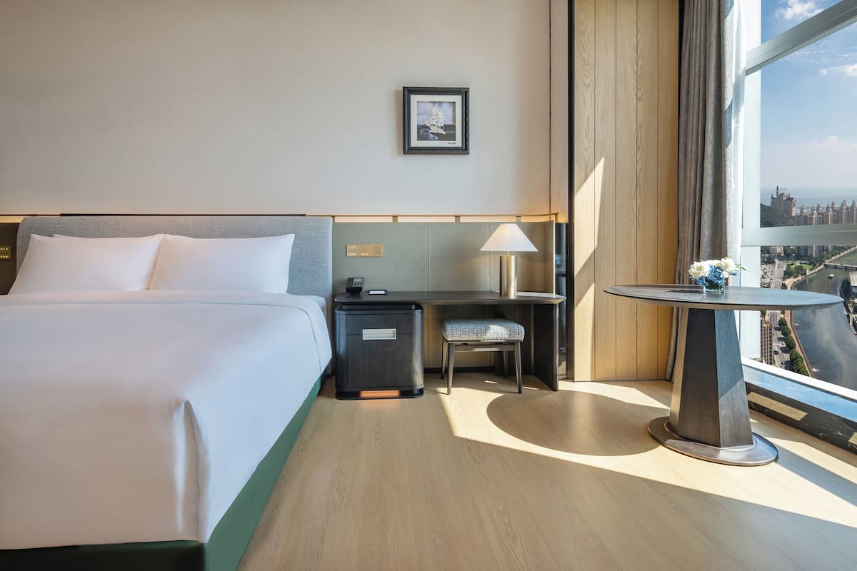Ein Hotelzimmer mit Bett, Schreibtisch, Stuhl, kleinem Tisch und Fenster mit Blick auf die Stadt.