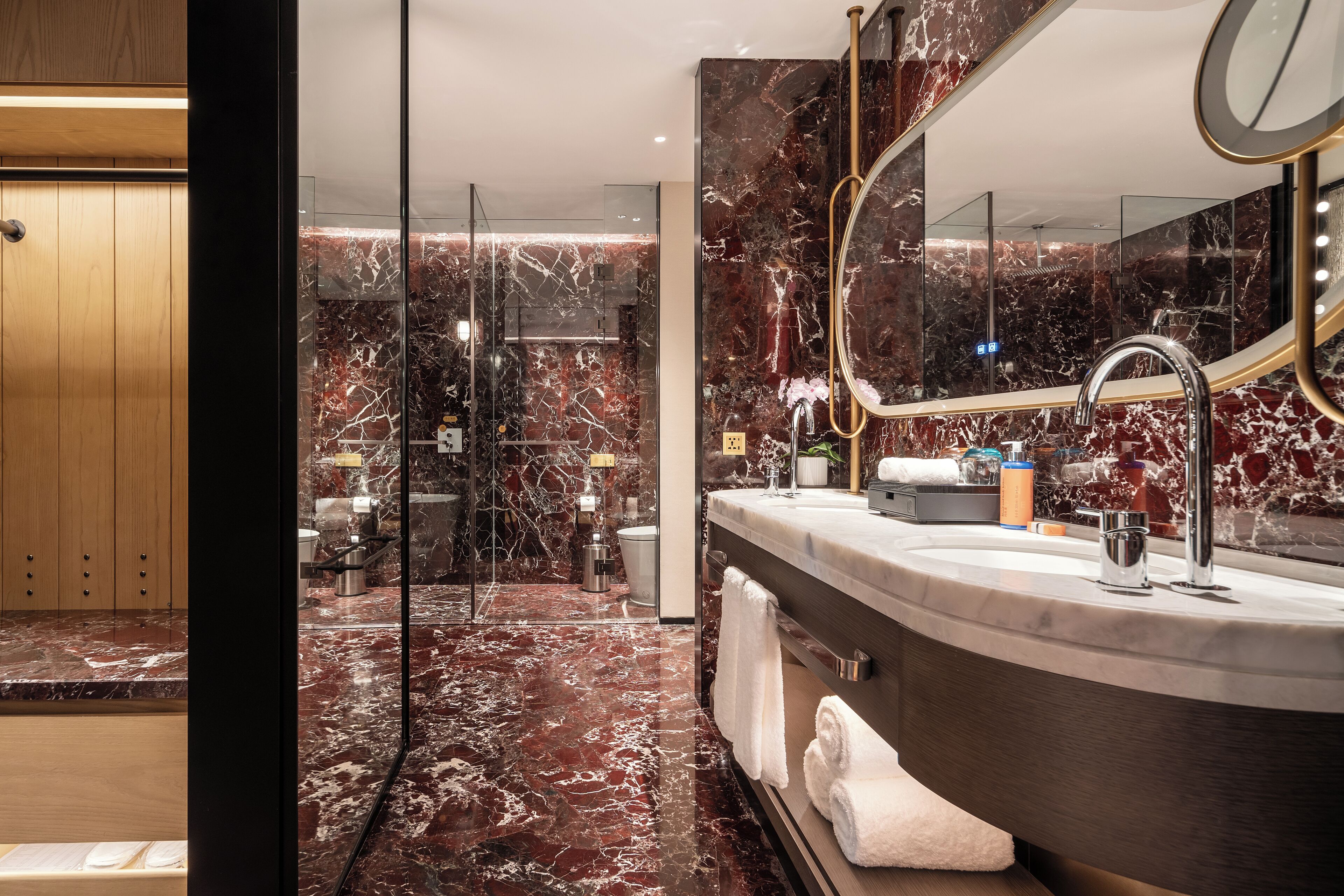 Une salle de bain moderne avec un sol en marbre, un meuble-lavabo aux lignes courbes, un grand miroir et une douche à parois de verre.