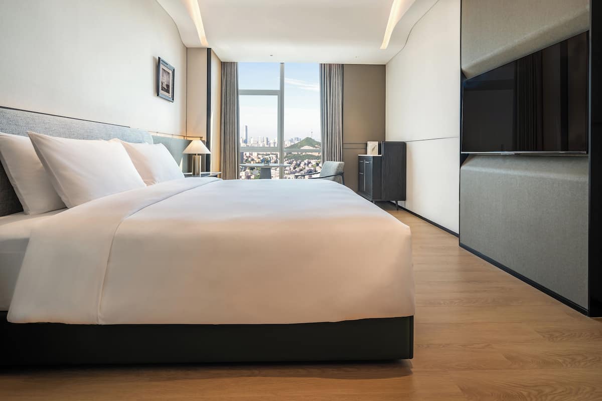 Ein modernes Hotelzimmer mit einem großen Bett, einem Fernseher, einem Schreibtisch und Blick auf die Stadt.