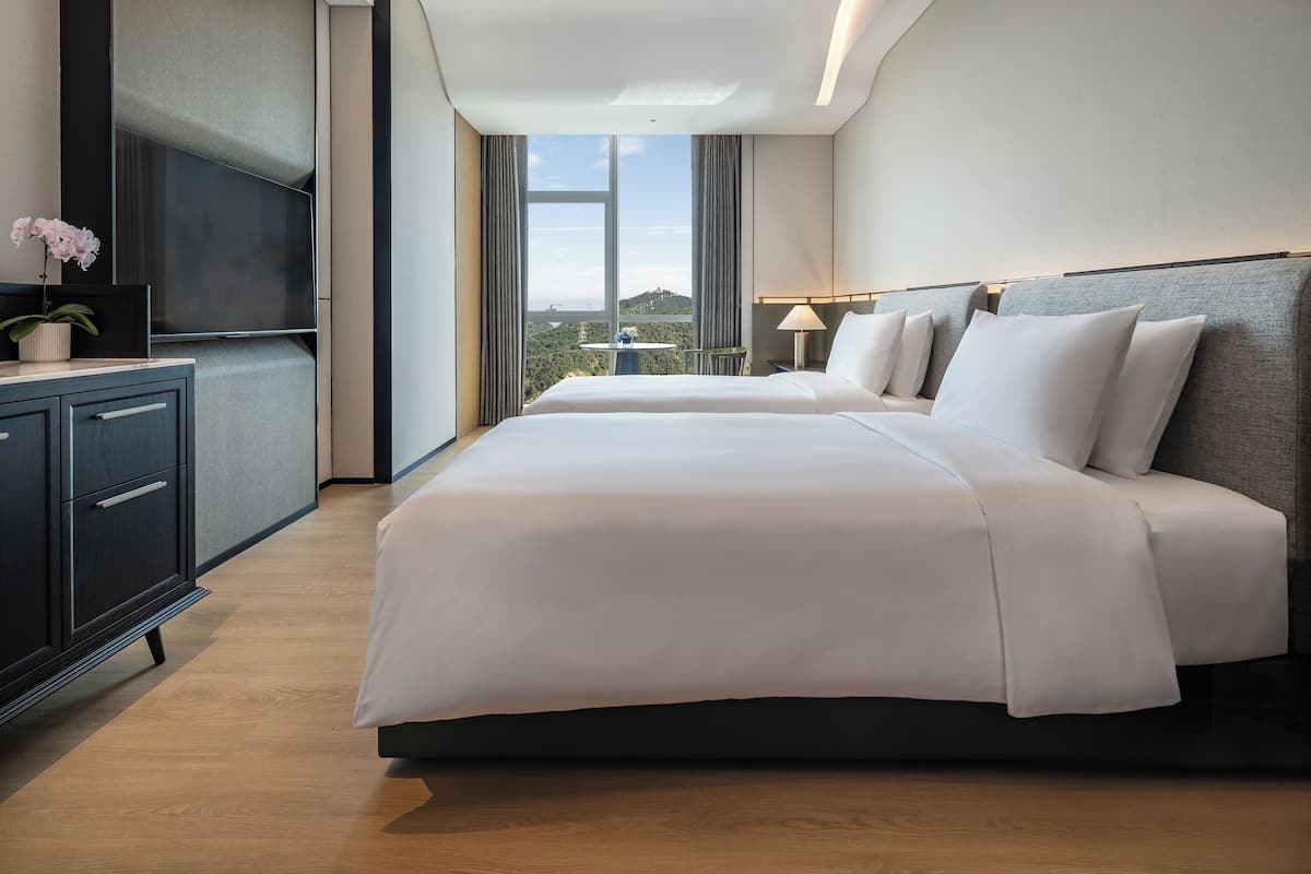 Ein modernes Hotelzimmer mit einem großen Bett, einem Fernseher, einem kleinen Tisch mit Lampe und Blick auf die Stadt.