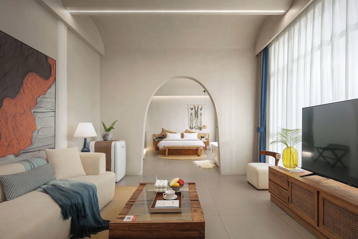 Una habitación de hotel moderna con una cama grande, un televisor y una mesita con frutas y una bandeja.
