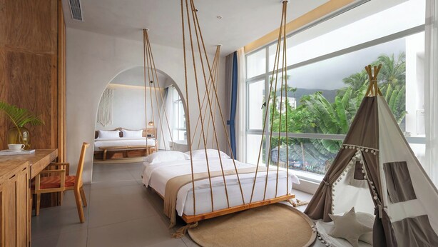 A modern bedroom with a large bed, a wooden desk, and a view of lush greenery. - TANG House (Wanning)