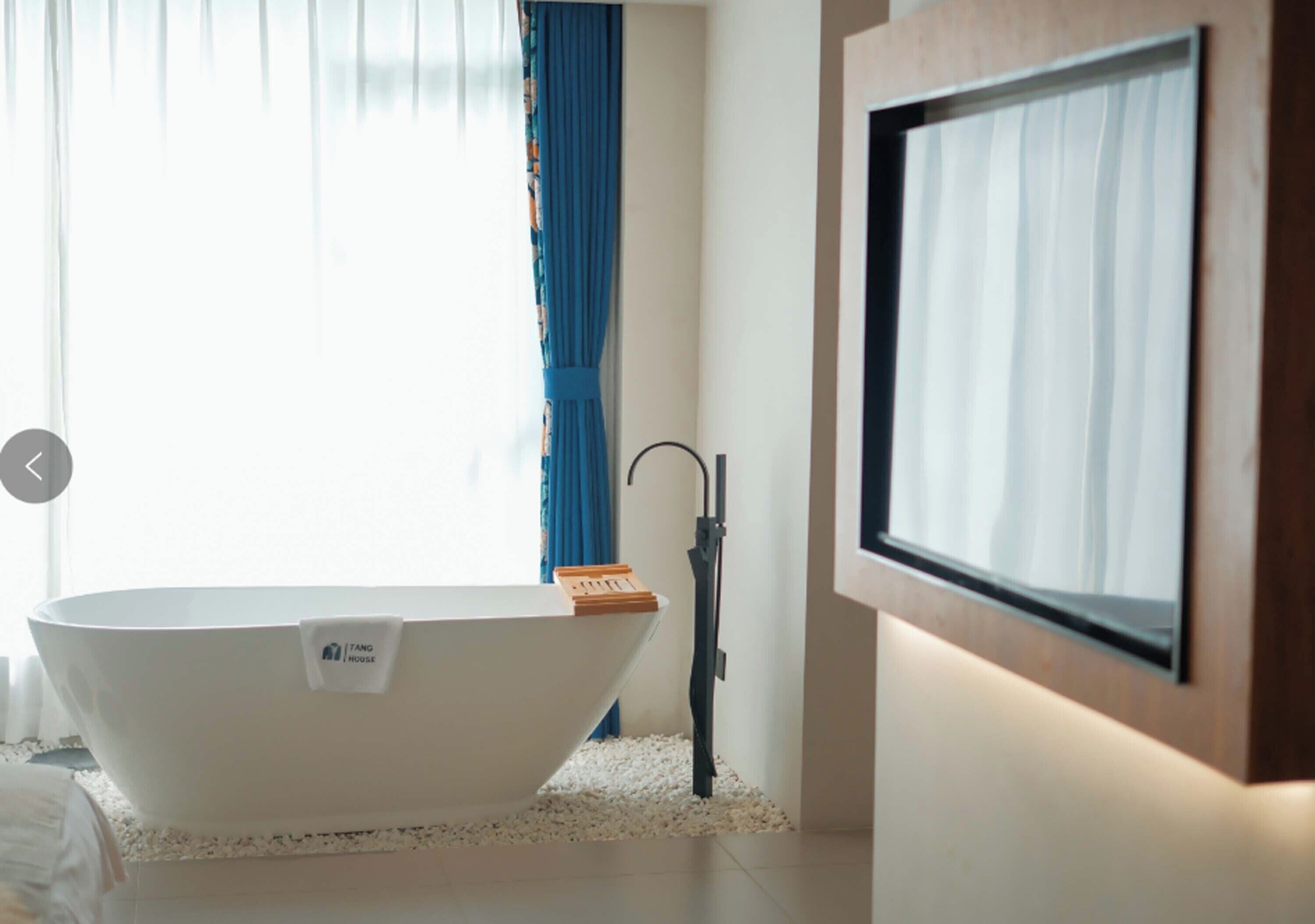 A modern bathroom with a freestanding bathtub, a wooden bath mat, and a towel rack.