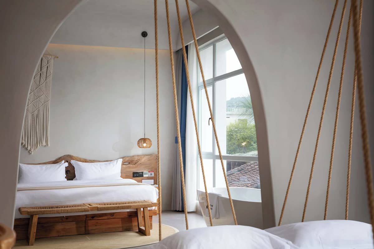 Un dormitorio con cama, mesita de noche, lámpara colgante y vistas al exterior.