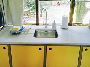 A kitchen with a sink, a dish rack, a toilet paper holder, and a window with a view of greenery. - 1 bedroom accommodation in Lavenham (Bury St Edmunds)