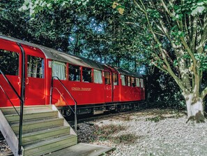 A red train with 'LONDON TRANSPORT' on the side, parked next to a tree and stairs. - 1 bedroom accommodation in Lavenham (Bury St Edmunds)