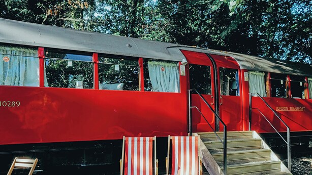 A red train with 'LONDON TRANSPORT' written on the side, a set of stairs leading to a platform, and two striped beach chairs. - 1 bedroom accommodation in Lavenham (Bury St Edmunds)