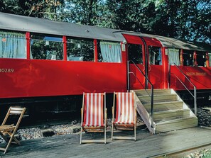 Un tren rojo con la inscripción 'LONDON TRANSPORT' en el lateral, unas escaleras que conducen a un andén, y dos sillas de playa a rayas.