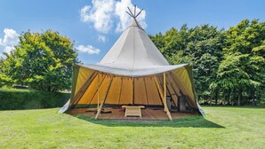 A large, conical tent with a wooden interior, set in a grassy field with trees in the background. - 1 bedroom accommodation in Lavenham (Bury St Edmunds)