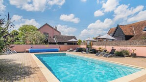A swimming pool with lounge chairs and umbrellas, surrounded by buildings with sloped roofs. - 1 bedroom accommodation in Lavenham (Bury St Edmunds)