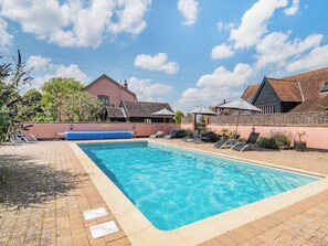 Ein Schwimmbecken mit Liegestühlen und Sonnenschirmen, umgeben von Gebäuden mit geneigten Dächern.