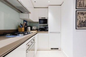 Una cocina moderna con armarios blancos, estufa a gas, microondas y cafetera.