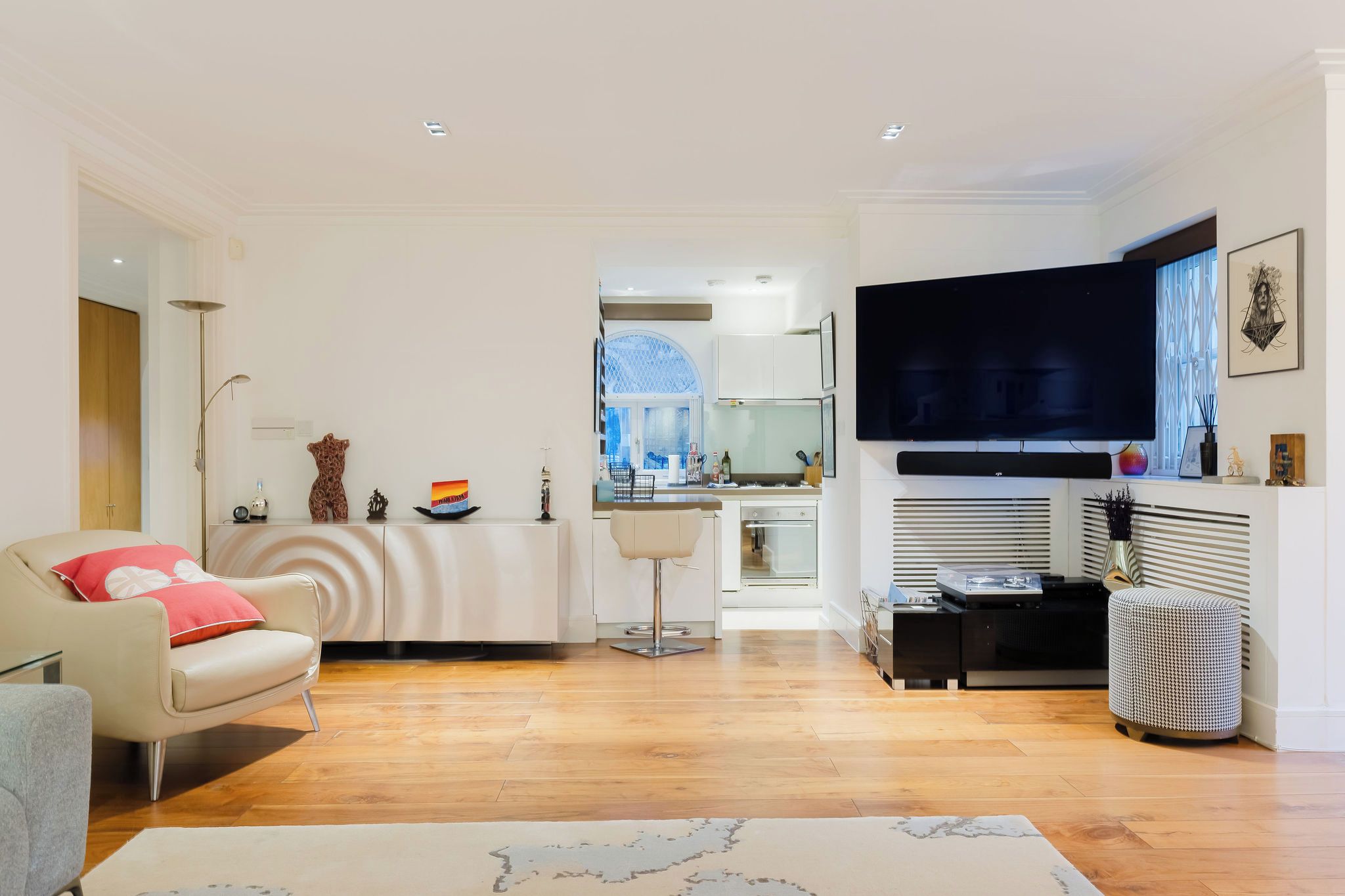 A modern living room with a sofa, a dining area, a kitchen, and a TV mounted on the wall.