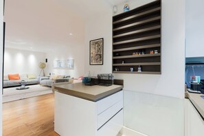 Ein modernes Wohnzimmer mit Sofa, Couchtisch und Essbereich mit Theke und Regalen.