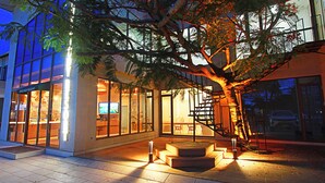 A modern hotel with a glass facade, outdoor seating area, and a staircase leading to an upper level. - Chez Judy Resort (Panglao)
