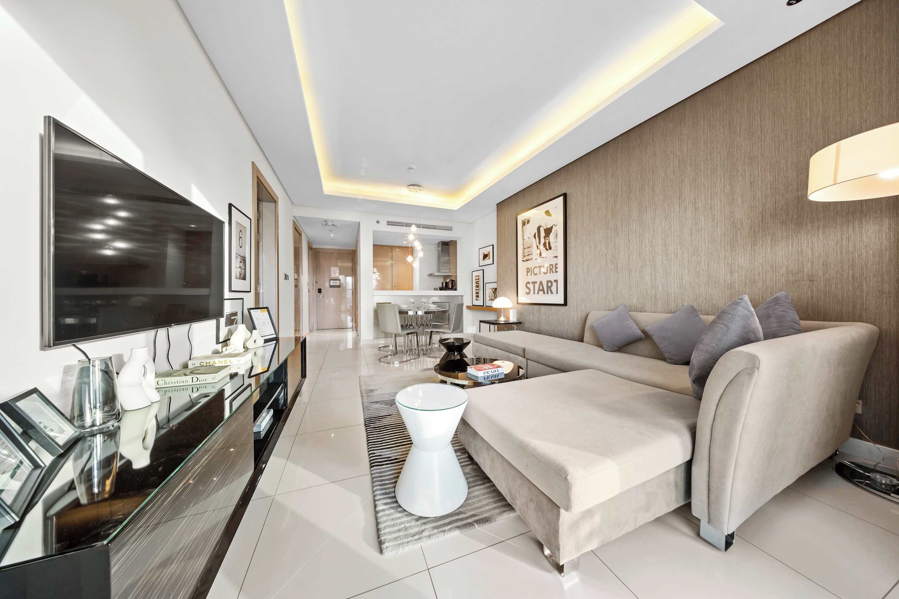 A modern living room with a sofa, a coffee table, and a TV. There is a kitchen area in the background.