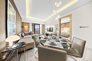 Una habitación de hotel moderna con zona de comedor, sofá, televisor y un espejo grande.