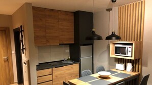 A compact kitchen with wooden cabinets, a black countertop, a microwave, and a dining area with a table and chairs. - Charmante Ferienwohnung in der Gemeinde Raska mit gemeinschaftlichem Parkplatz by Interhome (Kopaonik)