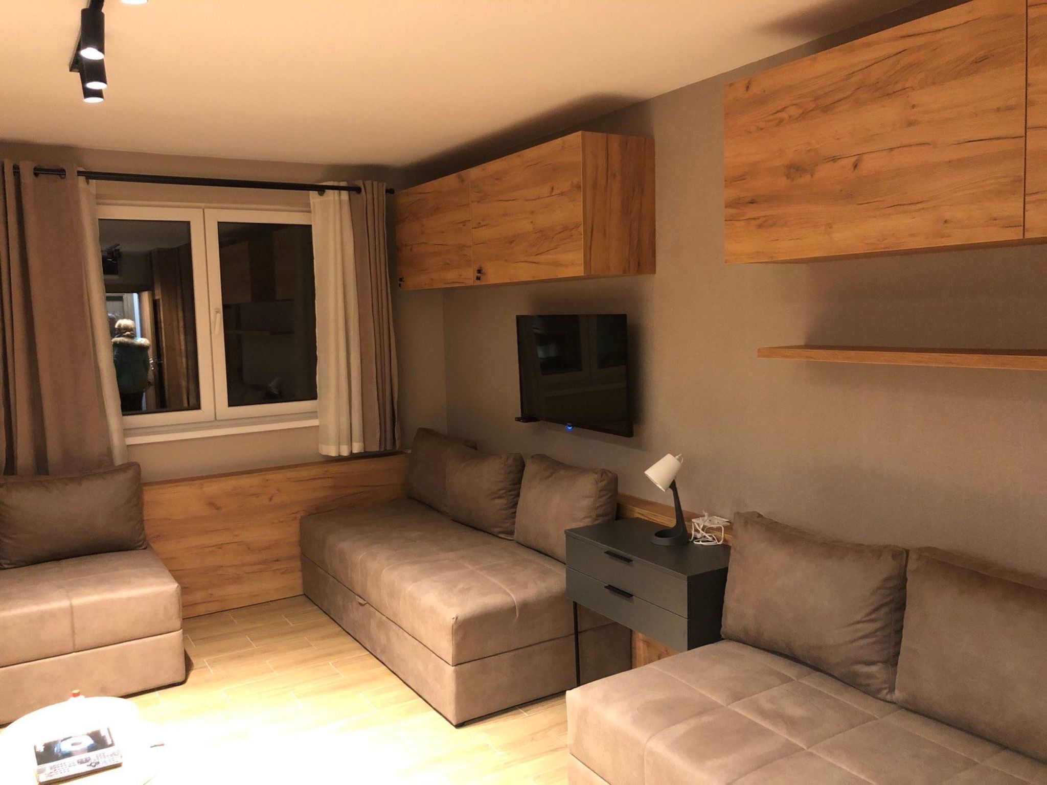 A modern living room with a sofa set, a TV mounted on the wall, and wooden paneling.