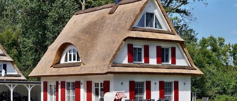 Uma casa tradicional com telhado de palha, paredes brancas e venezianas vermelhas.