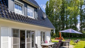 Talo, jossa on patio, ja patiolla on pöytä ja tuolit, satelliittiantenni sekä suuri aurinkovarjo.