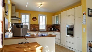 Una cocina con armarios blancos, una isla de madera, horno empotrado y cafetera.