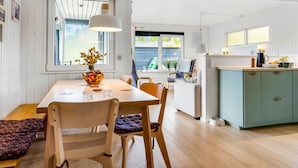 Eine moderne Küche mit Holzschränken, ein Essbereich mit Tisch und Stühlen sowie ein Blick ins Freie.