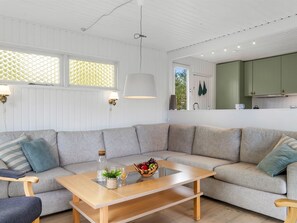 Una sala moderna con una mesa de centro de madera, un sofá gris y una cocina con armarios verdes.