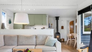 Ein modernes Wohnzimmer mit einer Couch, einem Couchtisch mit Früchten und einer Flasche, einem Kamin und einem Essbereich mit Stühlen.