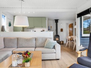 Una sala de estar moderna con un sofá, una mesita de centro con frutas y una botella, una chimenea y un comedor con sillas.