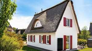 Une maison avec un toit à forte pente, des murs blancs et des volets rouges.