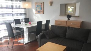 Ein modernes Wohnzimmer mit einer Couch, einem kleinen Holztisch und einem Essbereich mit Stühlen und einem Tisch.