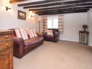 A living room with a brown leather sofa, a wooden chest of drawers, a plaid-patterned armchair, and a radiator.