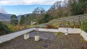Une terrasse sur le toit, dotée d’un mur en pierre, d’une rambarde en métal et offrant une vue sur le paysage environnant.