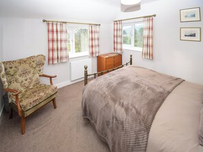 A bedroom with a bed, a chair, a dresser, and two windows with curtains.