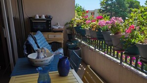 Un balcon avec une table jaune, des chaises bleues, un vase bleu et des plantes en pot.