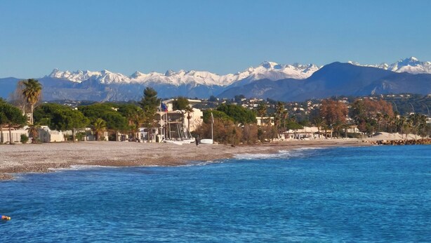 Un paysage côtier offrant une vue dégagée sur la mer, une plage et une chaîne de montagnes en arrière-plan.
